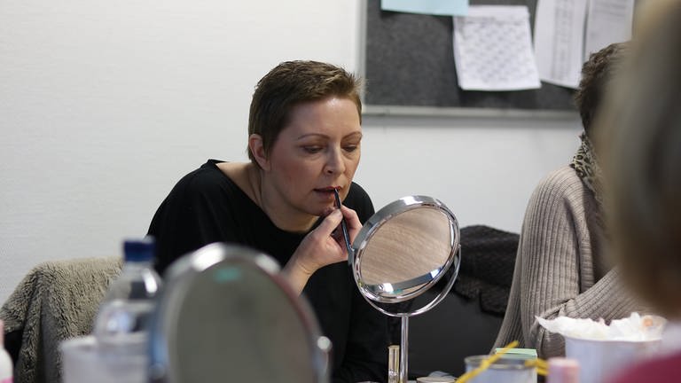 Eine Frau mit kurzen Haaren schminkt sich vor dem Spiegel die Lippen.