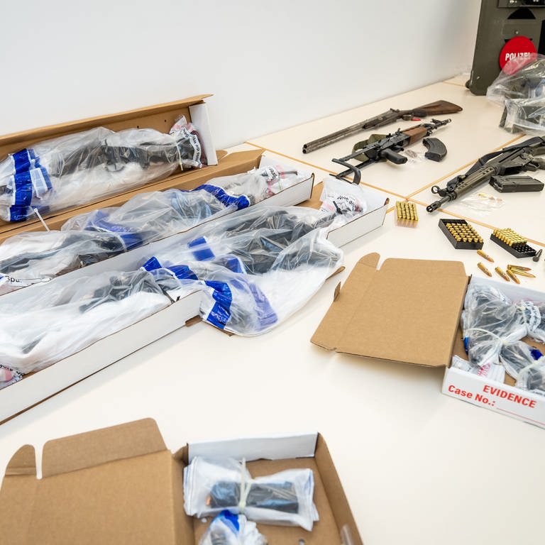 Beweismittel in Form von Waffen, die bei einem SEK-Einsatz in Boxberg (Main-Tauber-Kreis) sichergestellt wurden, liegen eingepackt in Plastikfolie auf einem Tisch im Polizeipräsidium Heilbronn. Zur Veranschaulichung liegen daneben typgleiche Waffen. 