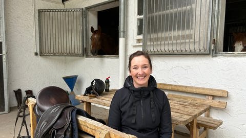 Die Vorsitzende des Reivereins in Aalen, der sich schon an die Polizeiverordnung hält und den Mist ihrer Tiere aufräumt, sitzt auf einer Bank vor einem Pferd im Stall. 